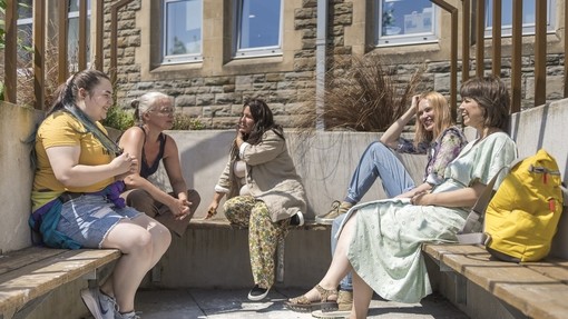 five students sitting on bench outside in the sun