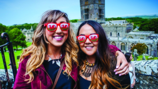 Students smiling in front of a castle wearing Welsh dragon sunglasses
