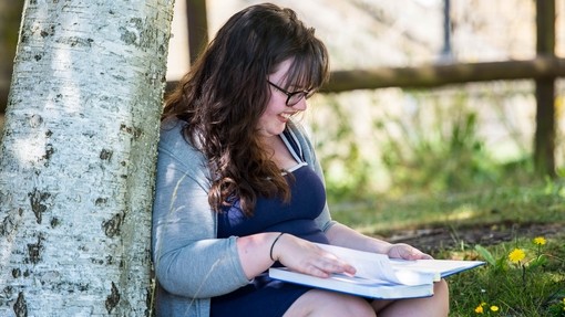 Student sitting against a tree and reading a book
