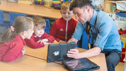 Teacher showing three primary students an educational video